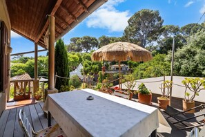 Eine Terrassensitzgelegenheit mit Tisch, Stühlen, einem Reedschirm und Blumentöpfen.