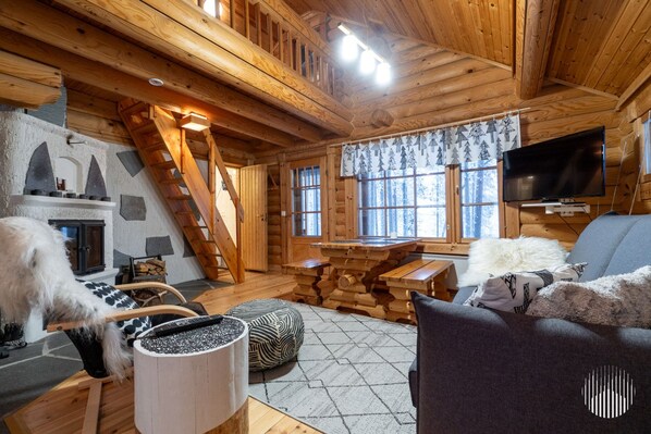 A cozy cabin interior with a fireplace, wooden furniture, a television, and a dog.