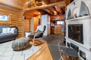 A log cabin interior with a sofa, a rocking chair, a fireplace, and a kitchen area.