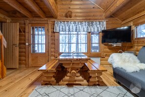 A log cabin interior with a wooden dining table, a sofa, and a television.