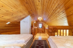 A log cabin interior with two beds, a hallway, and a window.