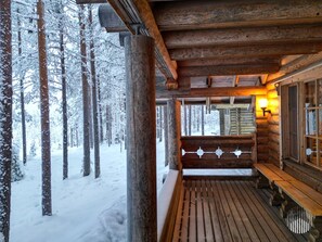A wooden cabin with a bench and a window overlooking a snowy forest.