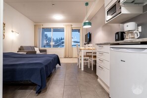 Ett hotellrum med en säng, ett skrivbord, ett litet kök och en tv.