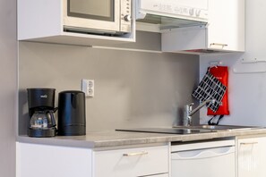 Eine Küche mit Mikrowelle, Kaffeemaschine und einer roten Schürze, die an der Wand hängt.