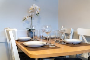 Ett matbord dukat med tallrikar, bestick och vinglas, och en vas med blommor hänger på väggen bakom.