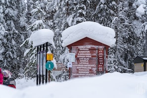 Ett snötäckt utomhusområde med en skylt som listar olika faciliteter och deras öppettider.