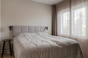 Un dormitorio con cama, mesita de noche y ventana con cortinas.