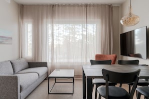 Ein modernes Wohnzimmer mit einer Couch, einem Couchtisch, einem Esstisch, Stühlen und einem an der Wand befestigten Fernseher.