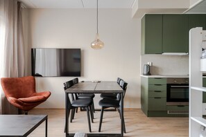 Een moderne woonruimte met een eettafel, stoelen, een bank, een flatscreen-televisie en een keuken met kastjes en apparatuur.
