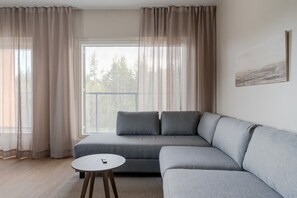 A modern living room with a grey sectional sofa, a round wooden coffee table, and sheer curtains. - Äkäsentie 1 A 313 by Holiday in Lapland (Äkäslompolo)