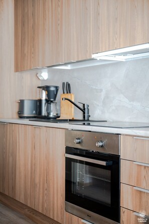 Une cuisine moderne avec des meubles en bois, un four en acier inoxydable, une machine à café et un bloc à couteaux.