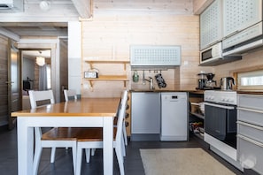 A compact kitchen with a wooden table, chairs, a refrigerator, a dishwasher, and a stove. - Revontuuli by Holiday in Lapland (Ylläs)