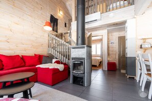 A cozy interior with a red sofa, a small table, a fireplace, and a staircase leading to an upper level. - Revontuuli by Holiday in Lapland (Ylläs)