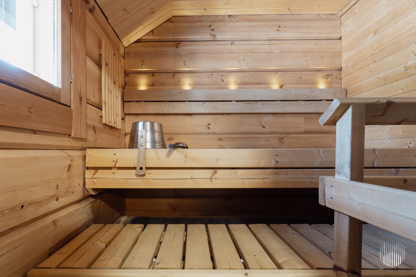 A wooden sauna with benches and a metal container, likely for water or steam.