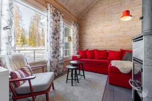 A cozy cabin interior with a red sofa, a wooden chair, a small table, and a fireplace. - Revontuuli by Holiday in Lapland (Ylläs)