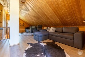 Une pièce mansardée chaleureuse avec un plafond en pente en bois, un canapé d’angle et un tapis en peau de vache.