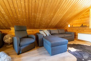 Une pièce mansardée accueillante, avec un plafond en pente, un canapé, un fauteuil, un ventilateur et un radiateur.