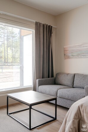 Ein modernes Wohnzimmer mit einem grauen Sofa, einem Holztisch und einem großen Fenster mit Vorhängen.