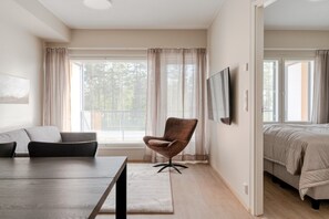 Ein modernes Schlafzimmer mit einem Bett, einem Sessel, einem Fernseher und einem Fenster mit Vorhängen.
