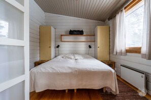 Ein Schlafzimmer mit einem Bett, einem Holzkopfteil, einem Regal über dem Bett, einem Fenster mit Vorhängen und einer Heizung.