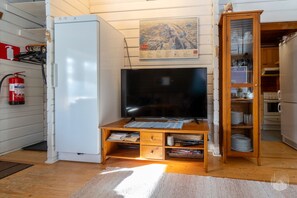 A compact living space with a television on a wooden stand, a small refrigerator, and a wooden cabinet with dishes. - Kelokaltiokylä 29 by Holiday in Lapland (Ruka)