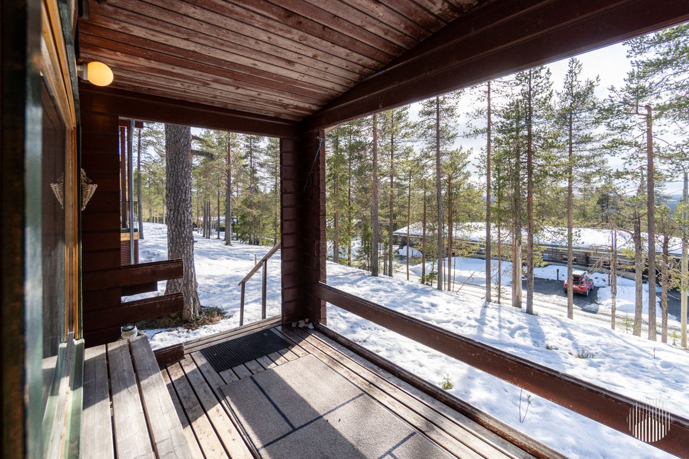 Una cabaña de madera con un porche, vista a un paisaje nevado y una escalera que da al exterior.