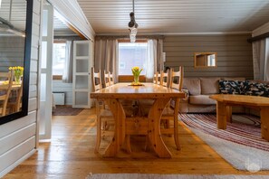 A dining area with a wooden table and chairs, a sofa, and a window with curtains. - Kelokaltiokylä 29 by Holiday in Lapland (Ruka)