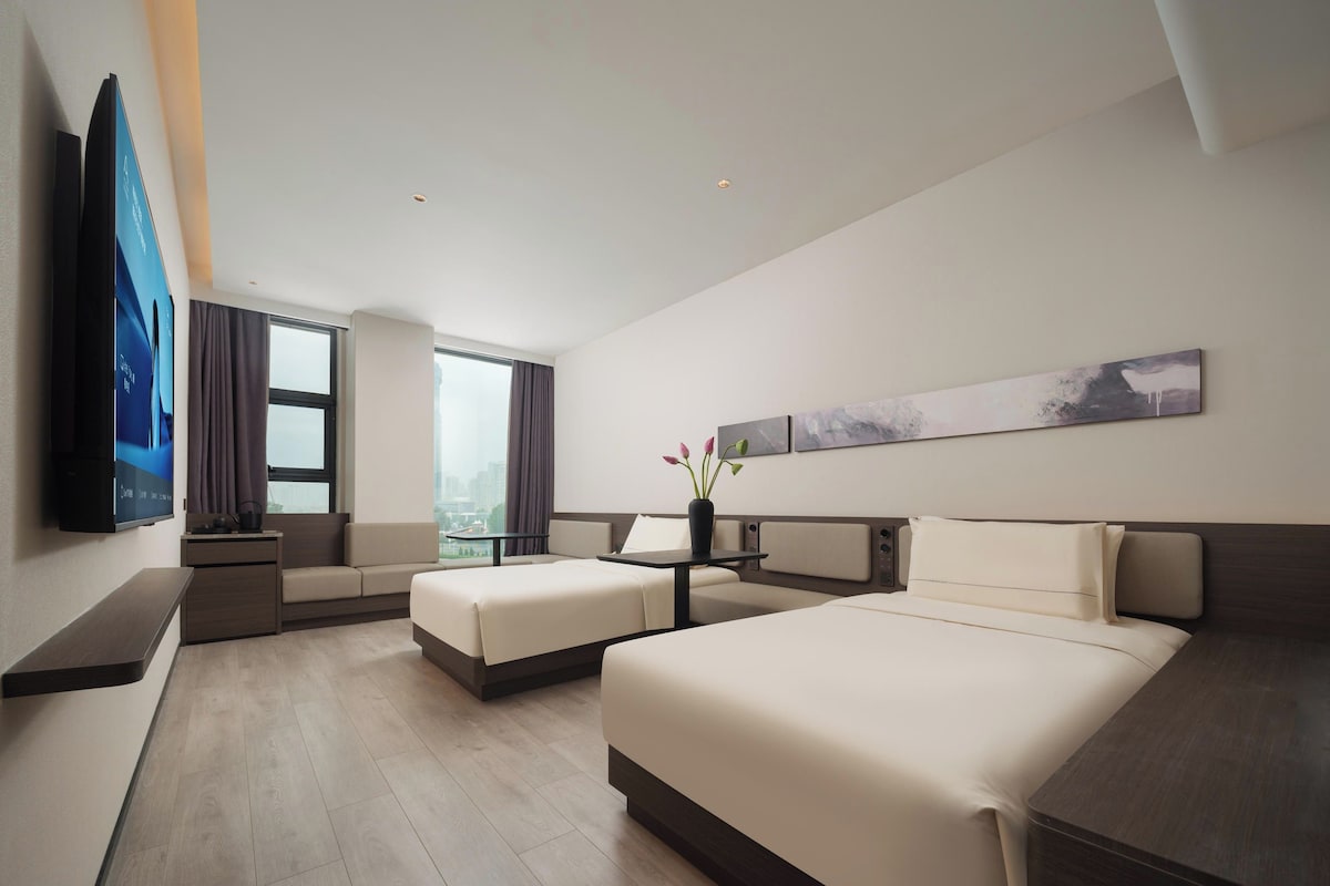 Et moderne hotelværelse med en stor seng, to små senge, et skrivebord og et fjernsyn.