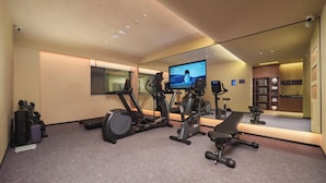 Ein Heimfitnessraum mit Trainingsgeräten, einem Fernseher und einem großen Spiegel.