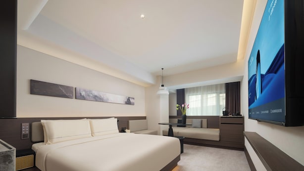 Ein modernes Hotelzimmer mit einem großen Bett, einem Schreibtisch, einem Sessel, einem Flachbildfernseher und Kunstwerken an den Wänden.