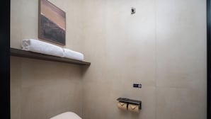 Ein Badezimmer mit Toilette, Handtuchhalter mit Handtuch, Toilettenpapierhalter und einer Wandleuchte.