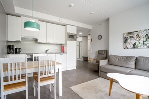 Een moderne keuken met witte kasten, een eettafel met stoelen, een grijze bank en een klok aan de muur.