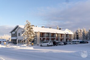 Um hotel com vários andares, teto coberto de neve, diversas varandas e estacionamento com vários veículos.