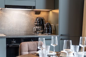 Une cuisine moderne équipée d’une machine à expresso et d’une cafetière intégrées, d’un lave-vaisselle et d’un coin repas avec une table dressée pour deux personnes.