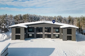 A modern building with a flat roof, multiple windows, and a snow-covered landscape. - Metsonlinna 205 by Holiday in Lapland (Levi)