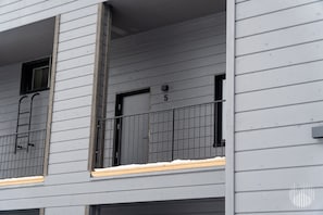 Ein mehrstöckiges Gebäude mit grauer Fassade, nummerierten Fenstern und einem Metallgeländer.