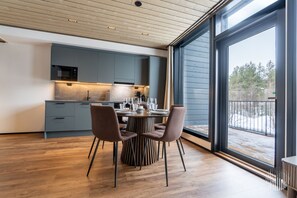 A modern kitchen with a dining area, large windows, and a view of a snowy landscape. - Metsonlinna 205 by Holiday in Lapland (Levi)