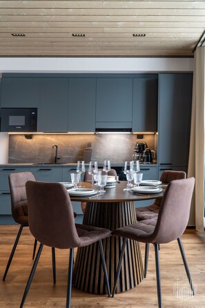Une cuisine moderne avec des meubles de couleur sombre, un four à micro-ondes encastré et un coin repas comprenant une table ronde et quatre chaises.