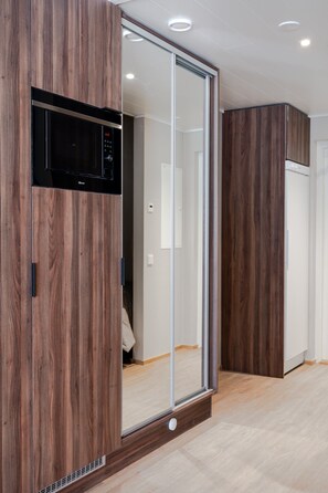 Ein moderner Kleiderschrank mit integriertem Mikrowellenherd, einer schiebbaren Spiegeltür und Holzoptik.