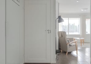 A modern room with a white door, a grey armchair, a small table, and a lamp. - Sivulantie 4 202 by Holiday in Lapland (Äkäslompolo)