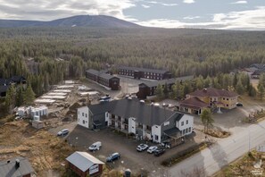 Vue aérienne d’un ensemble immobilier commercial comprenant plusieurs bâtiments, des aires de stationnement et un paysage boisé en arrière-plan.