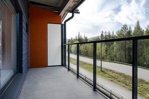 A balcony with a metal railing, a door, and a view of a road and forest. - Äkäsentie 1 A 305 by Holiday in Lapland (Äkäslompolo)