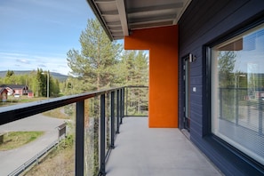 A balcony with a metal railing, a concrete floor, and a view of a red building and trees in the background. - Äkäsentie 1 A 305 by Holiday in Lapland (Äkäslompolo)