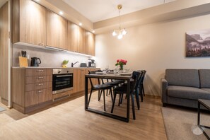 Eine moderne Küche mit Holzausbau, einem Esstisch mit Stühlen und einem grauen Sofa im Wohnbereich.