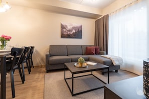 Ein modernes Wohnzimmer mit einem grauen Sofa, einem Couchtisch und einem Essbereich mit Stühlen und einem Tisch für zwei Personen.