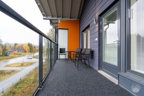Un balcon avec une table et des chaises, une vue sur une route et des immeubles, et une rambarde en verre.