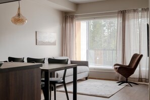 Ein modernes Wohnzimmer mit Essbereich, einer Couch, einem Sessel und einem großen Fenster mit Vorhängen.