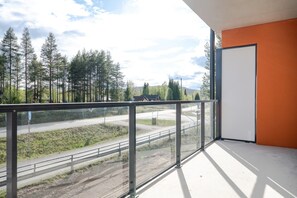 Ein Balkon mit Blick auf eine Straße und Bäume, eine Glastür und ein Metallgeländer.