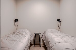 Ein Zimmer mit zwei Betten, einem kleinen Hocker und zwei Wandleuchten.
