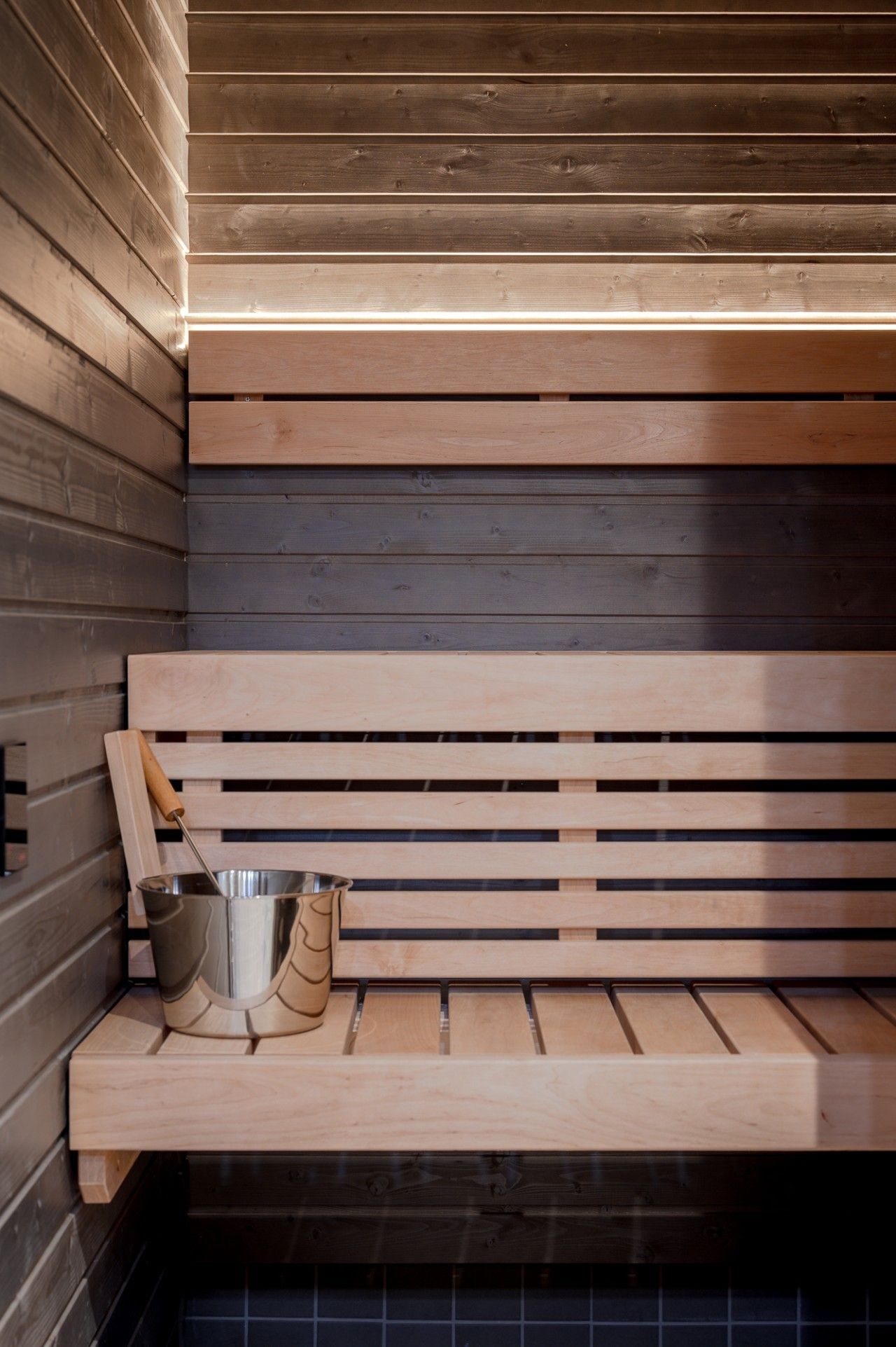 A wooden sauna bench with a metal bucket and a wooden tool.